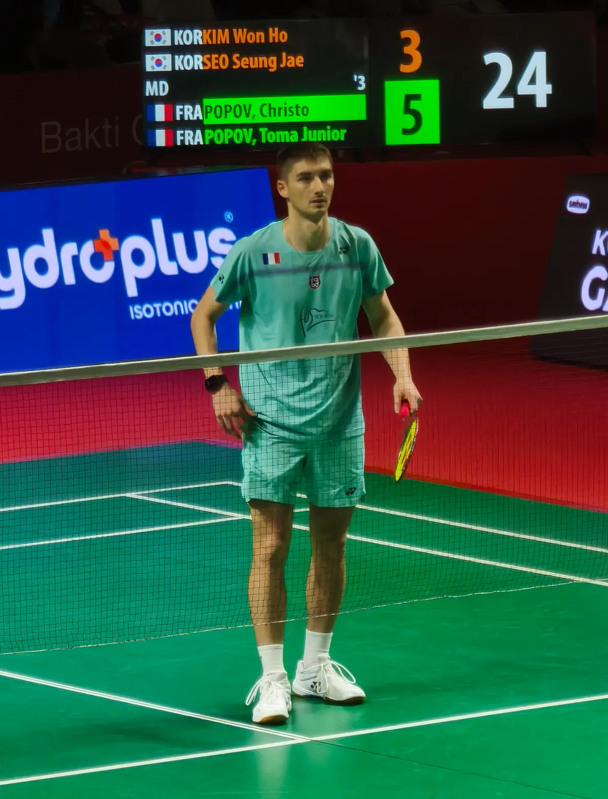 Christo Popov, en tenue vert menthe frappée du drapeau français, raquette à la main près du filet sur un court vert.